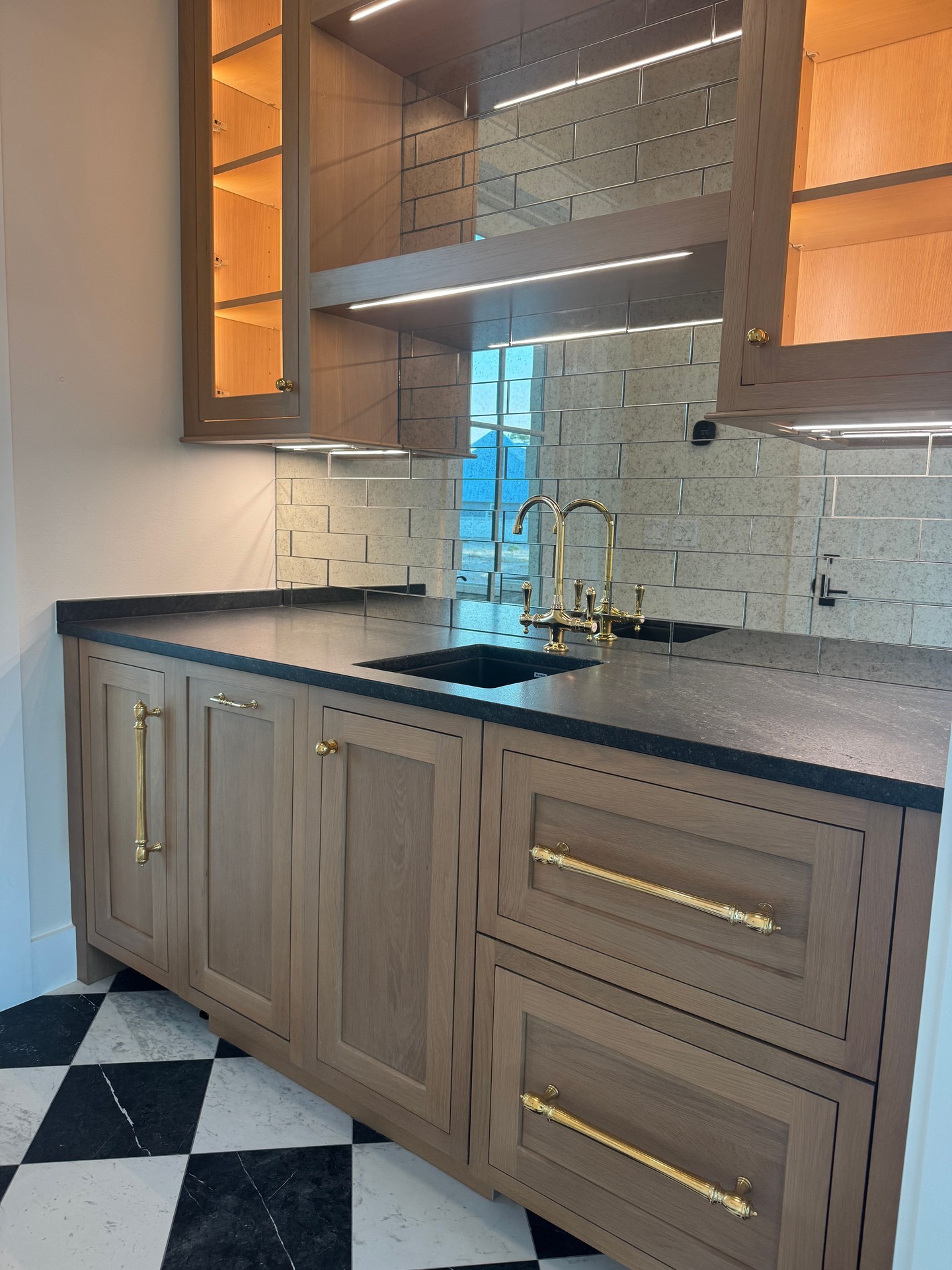 A sophisticated blend of style and function. This custom bar features warm wood cabinetry, mirrored tile, brass accents, and a striking black-and-white floor that adds timeless character. Thoughtful details like these are a hallmark of every Huff home in @watersoundorigins.